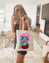 Load image into Gallery viewer, Person holding a cute halloween alien girl tote bag with a colorful character design in a living room.