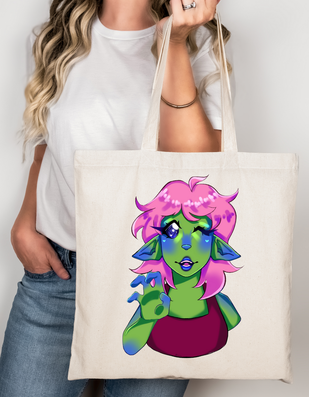 Person holding a tote bag with a colorful character design on a plain background